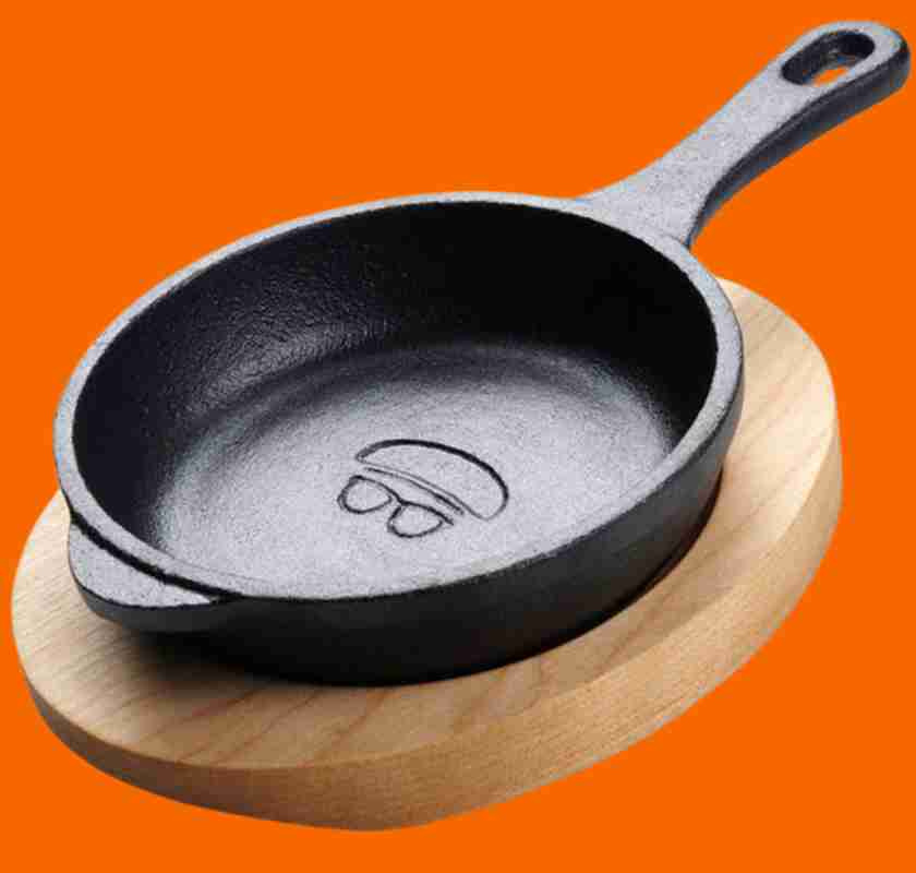 Minipanna i gjutj�rn med underl�gg i tr� mot orange bakgrund